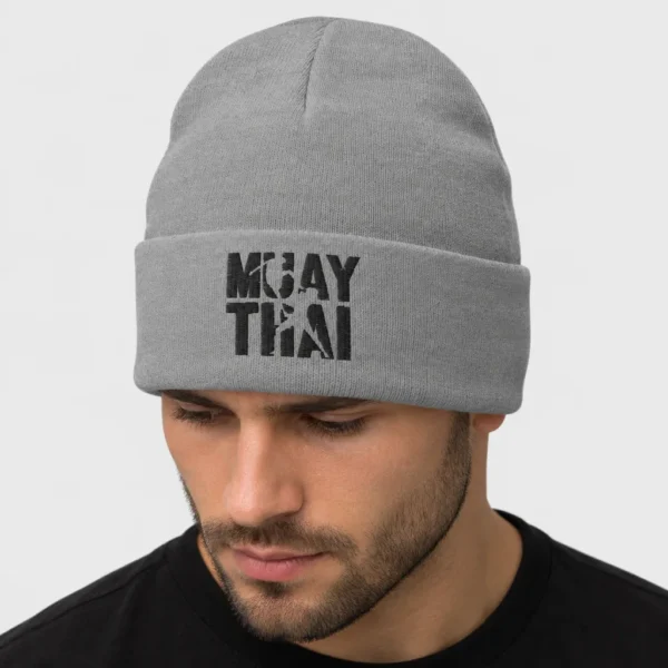 Bonnet ajusté brodé devant du texte noir « MUAY THAI » sur deux lignes, découpé par les silhouettes de deux combattants dont l'un place un coup de genou sauté. – photo studio