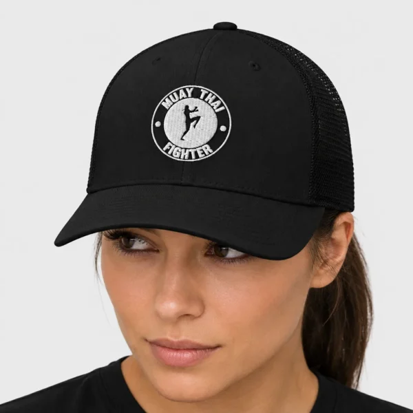 Casquette trucker rétro brodée sur le devant d'un badge circulaire avec la silhouette d'une combattante de muay-thaï genou levé et le texte « MUAY THAI FIGHTER ». – photo studio femme