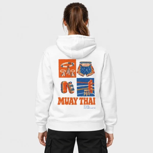 Sweat à capuche clair imprimé d'une illustration vintage de mongkol, short thaï, paos et coin de ring au-dessus du titre orange « MUAY THAI ». – photo studio femme