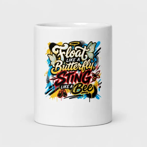 Mug blanc brillant imprimé de la citation « Float like a Butterfly, Sting like a Bee » en lettrage graffiti, avec papillons, abeille et gants de boxe sur fond d'éclaboussures jaunes, bleues et noires. – photo studio