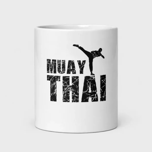 Mug blanc brillant imprimé de la silhouette noire d'un combattant de muay-thaï en high kick au-dessus du lettrage « MUAY THAI » à effet craquelé. – photo studio