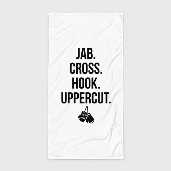 Serviette de plage blanche imprimée des mots « JAB. CROSS. HOOK. UPPERCUT. » en lettres capitales empilées au-dessus d'une paire de gants de boxe suspendus. – photo studio