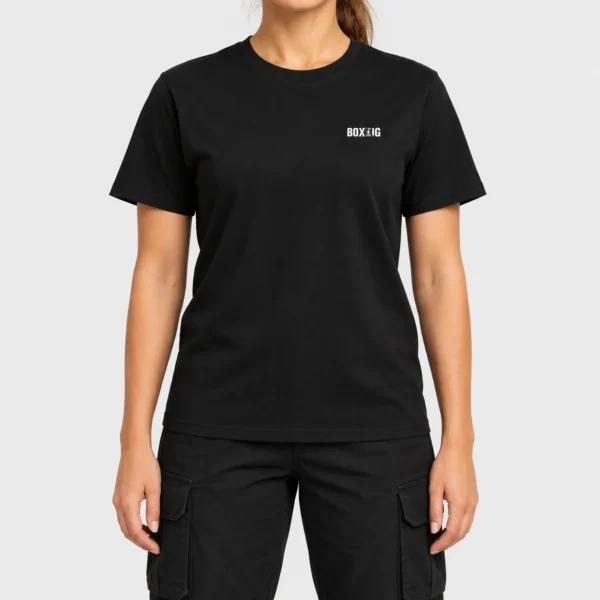 T-shirt unisexe avec, côté cœur, le mot « BOXING » en lettres noires où deux silhouettes de boxeurs en plein échange sont découpées en négatif dans le « I » et le « N ». – photo studio femme