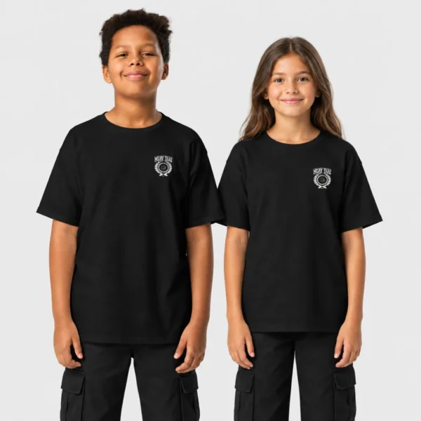 T-shirt enfant orné côté cœur d'un écusson vintage « MUAY THAI » avec poing fermé, couronne de lauriers, étoiles et banderole façon varsity. – photo studio